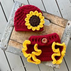 two crocheted hats with yellow and red flowers on them sitting on a wooden crate