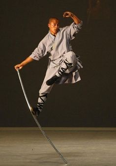 a man in grey shirt doing tricks on metal pole with one leg and two hands