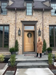 a woman standing in front of a stone house with a wreath on it's door