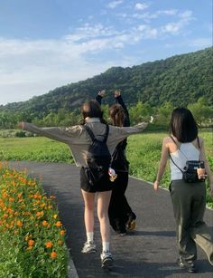 three people walking down a path with their arms in the air and one person holding her hands up