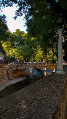 an old stone bridge over a small stream in a park with people walking on it