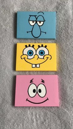 three cartoon faces painted on canvases in different colors