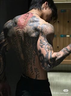 a man with lots of tattoos on his back and arm holding a cell phone in front of him