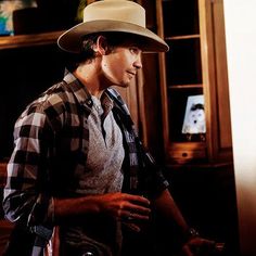 a man wearing a hat standing in front of a book shelf