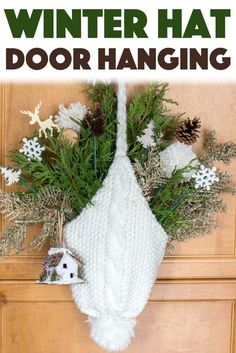 a knitted hat hanging on the front door with pine cones and evergreens around it