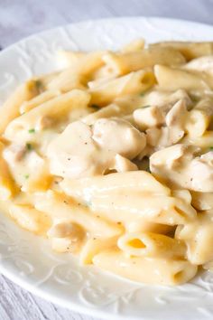 a white plate topped with pasta covered in chicken and cream sauce on top of a wooden table