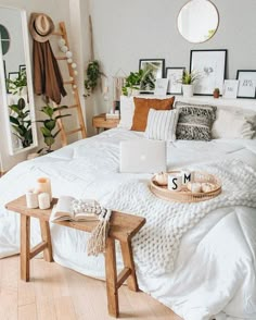 a bed with white sheets and pillows in a bedroom next to a wooden ladder, potted plants and pictures on the wall