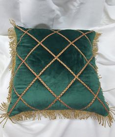 a green and gold pillow with tassels on the edges, sitting on a white bed