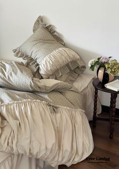 there is a bed with many pillows and blankets on it, along with a small side table