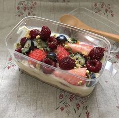 a glass dish filled with fruit and nuts on top of a table cloth next to a wooden spoon