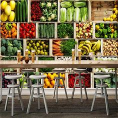 a large display of fruits and vegetables on a wall behind two tables with stools