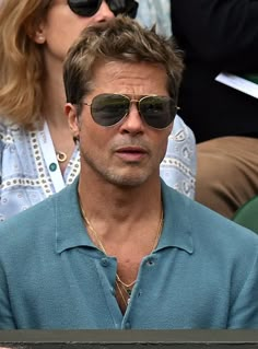 a man wearing sunglasses sitting in the stands at a tennis match with other people behind him