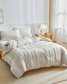 a bed with white comforter and pillows in a room next to a large window