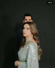 a man and woman standing next to each other in front of a black wall with the words on it