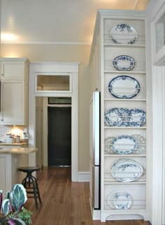 a narrow kitchen with white cabinets and blue plates on the shelves, along with hardwood flooring