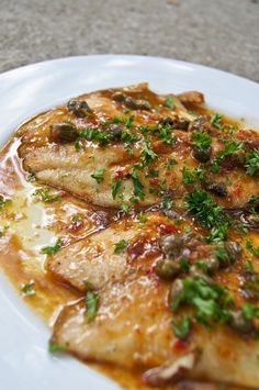 a white plate topped with fish covered in sauce and garnished with parsley