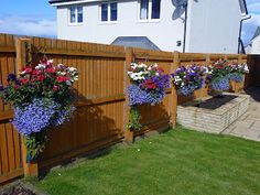 three hanging flower baskets on the side of a wooden fence in front of a house