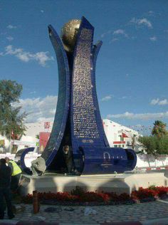 a large blue sculpture in the middle of a park with people standing around and looking at it