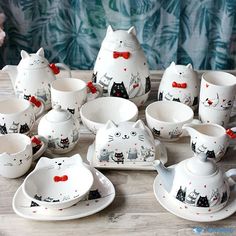 a table topped with lots of white dishes and cups filled with cat themed food items