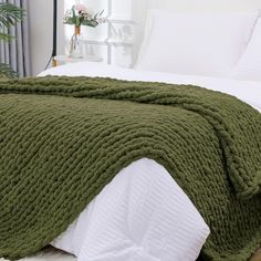 a large green blanket on top of a bed next to a white comforter and pillows