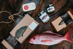 some fish are laying on the table next to boxes with labels and other items around them