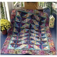 a colorful quilt is on the porch next to a potted plant and birdhouse