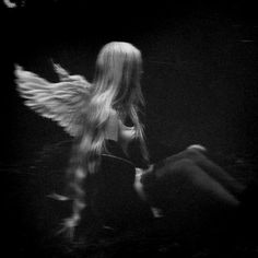 a black and white photo of a woman with angel wings on her back, in the dark