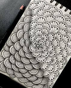 a spiral notebook with an intricate design on the front and back cover, next to a pencil