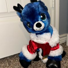 a blue and white stuffed animal wearing a red outfit sitting on the floor next to a door