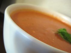 a white bowl filled with soup and garnished with a green leaf on top