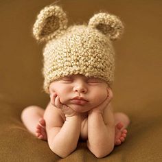 a baby wearing a crocheted hat laying on top of a brown blanket with his hands under his chin