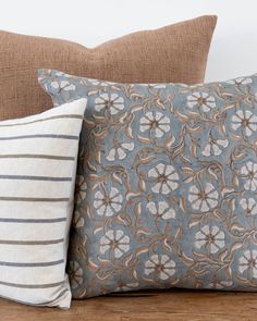 two decorative pillows on a couch in front of a white wall and wood flooring