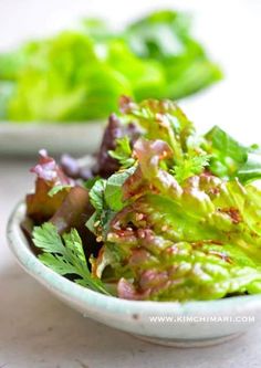 a white bowl filled with lettuce on top of a table next to another plate