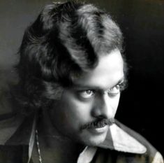 a black and white photo of a man with long curly hair wearing a collared shirt