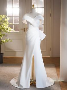 a white wedding dress on display in front of a door with a potted plant