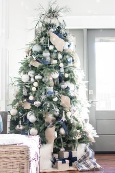 a white christmas tree with blue and silver ornaments on it in a living room next to a wicker basket