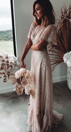 a woman standing in front of a window wearing a long dress and holding a bouquet