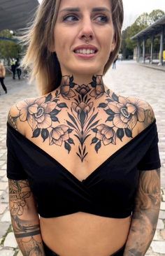 a woman with tattoos on her chest posing for the camera in front of a building