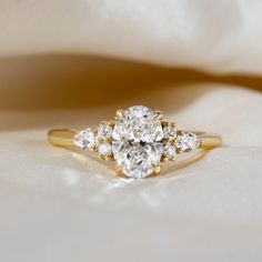 an oval diamond ring with three smaller diamonds around it on a white satin cloth background