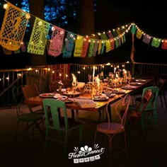 an outdoor dining table set up with colorful lights and decorations on the string above it