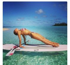 a woman on a surfboard in the ocean with her legs spread out and head down