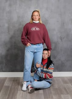 two people standing next to each other in front of a gray wall and wood floor