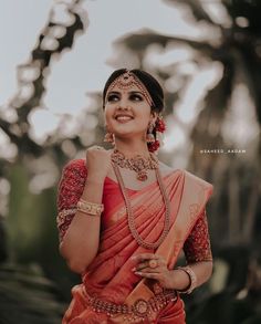 a woman in an orange and red sari is posing for the camera with her hands on her hips