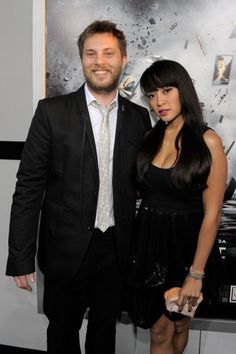 a man and woman standing next to each other in front of a poster on the wall