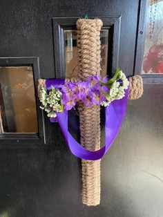 a cross made out of rope with purple flowers on the top and blue ribbon tied to it