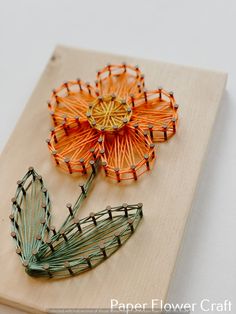 two paper flowers sitting on top of a wooden board