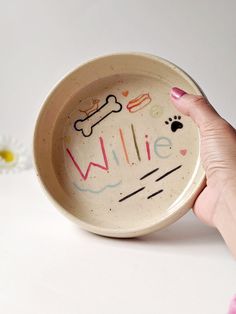 a person's hand holding a small bowl with the word willie painted on it