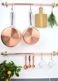 copper pots and pans hanging on a wall with kitchen utensils in the foreground