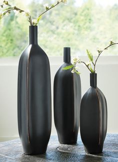 three black vases sitting on top of a table next to each other with flowers in them