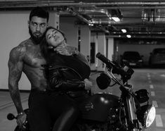 a man and woman sitting on a motorcycle in a parking garage with their arms around each other